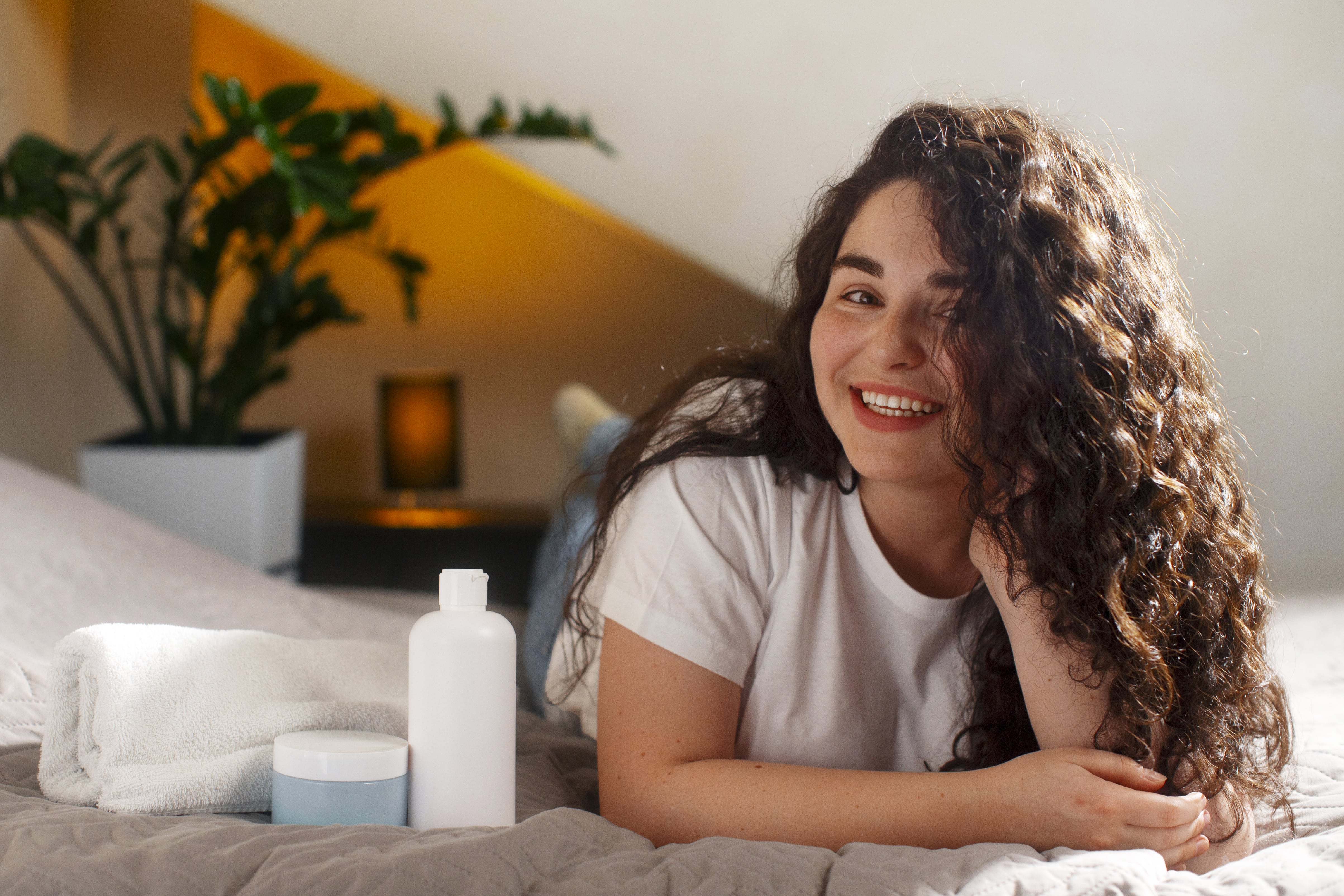 A curly-haired woman relaxes with shampoo and conditioner nearby.