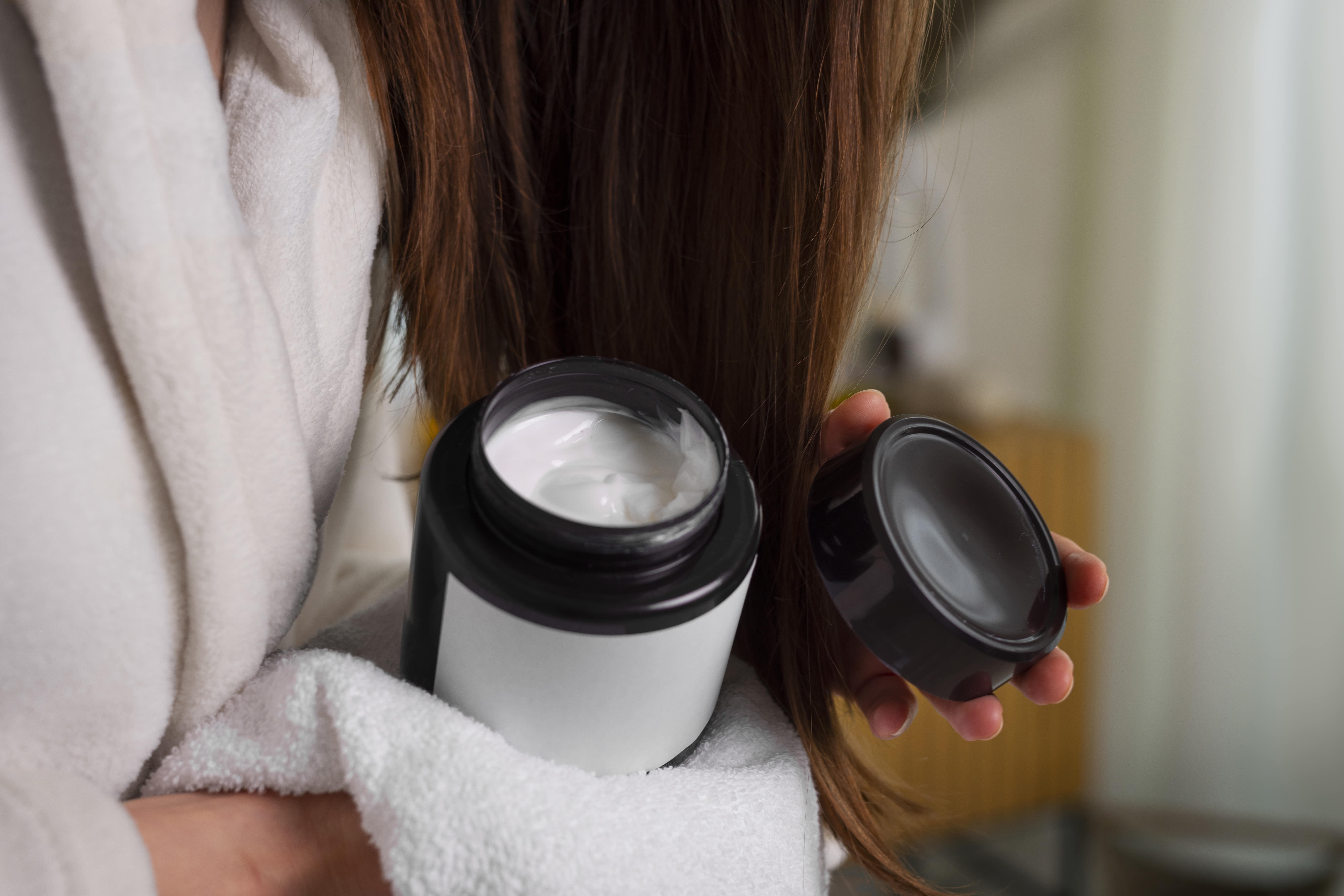 A woman holds a bottle of conditioner, showcasing her hair care routine.